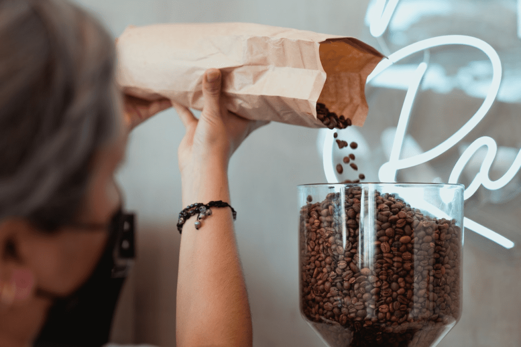 Mulher colocando grãos de café em um recipiente. Fonte: Pexels