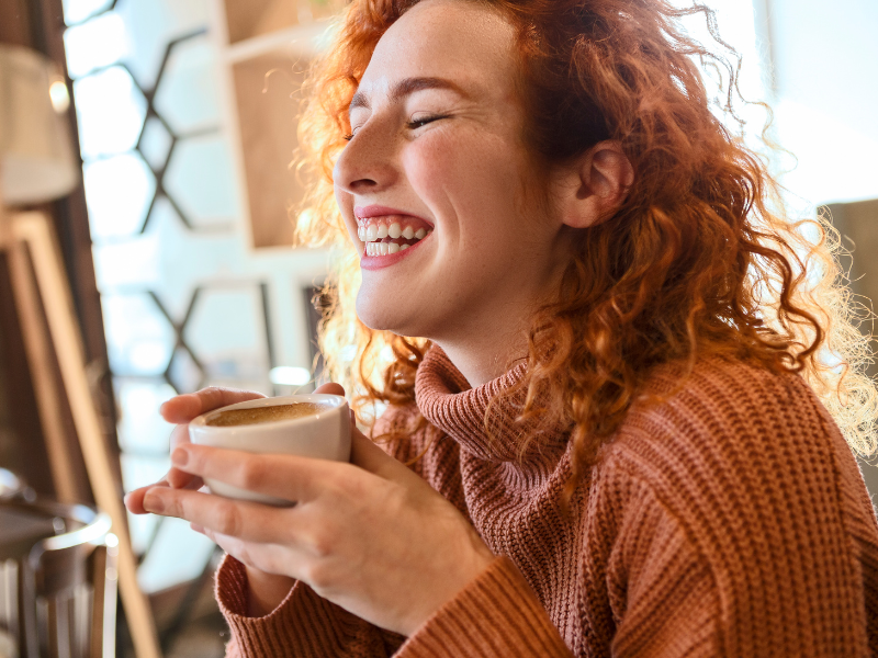 Mulher tomando café e sorrindo. Foto: Nastasic de Getty Images Signature - Canva